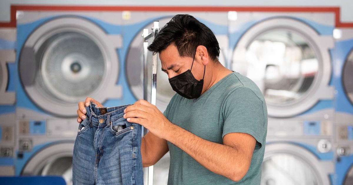 Man wearing mask washes jeans at laundromat