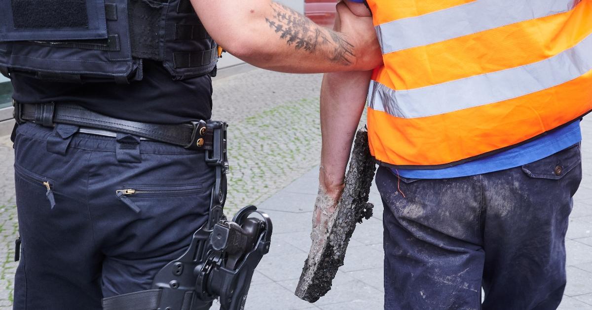 A police officer arrests a climate activist who still has his hand attached to concrete. 