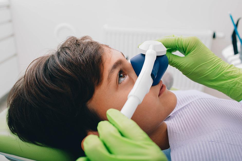 Small boy being given inhalation treatment at a dental clinic by a person with green gloves. 