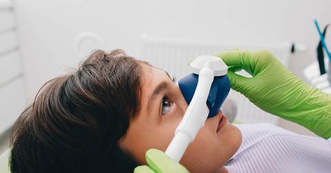 Small boy being given inhalation treatment at a dental clinic by a person with green gloves.