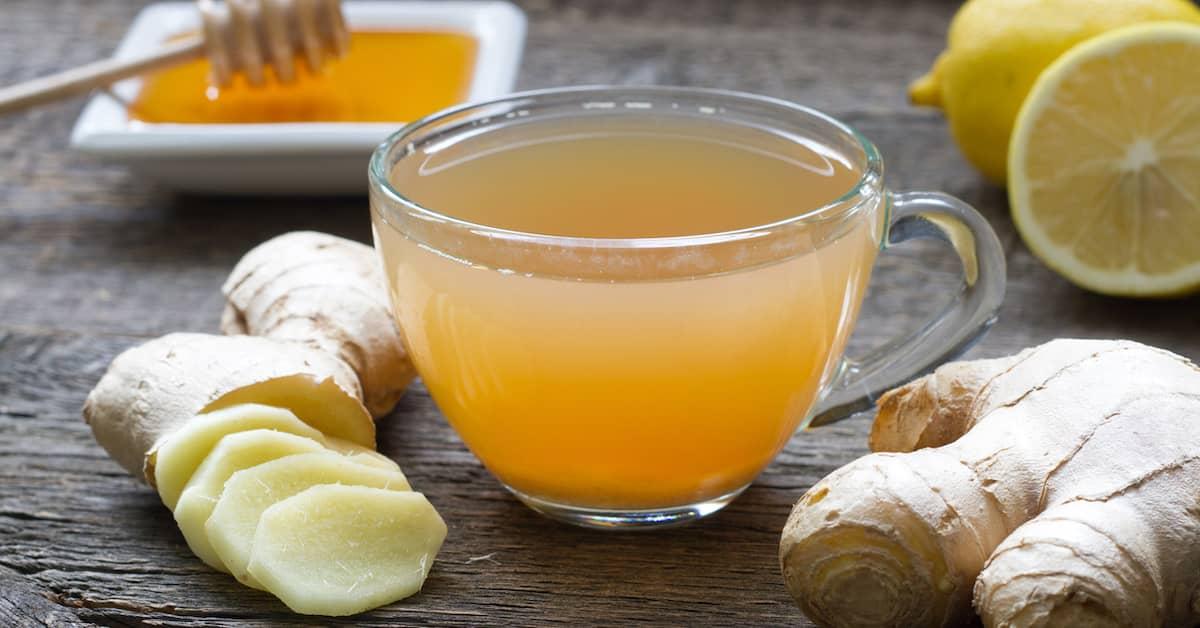 Cup of ginger tea on a wooden table surrounded by fresh ginger, lemon and honey