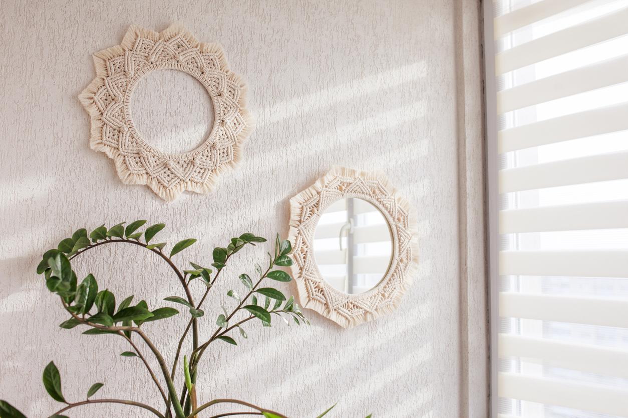 Two small, round macrame mirrors handing on a white wall diagonally from one another. 