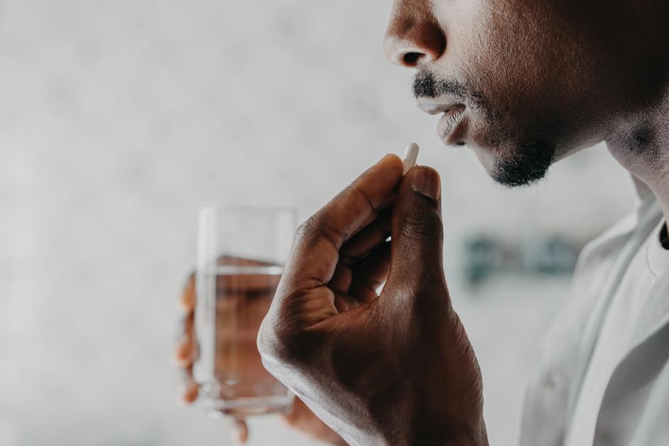 A close up of a man holding a glass of water and a pill to his mouth. 