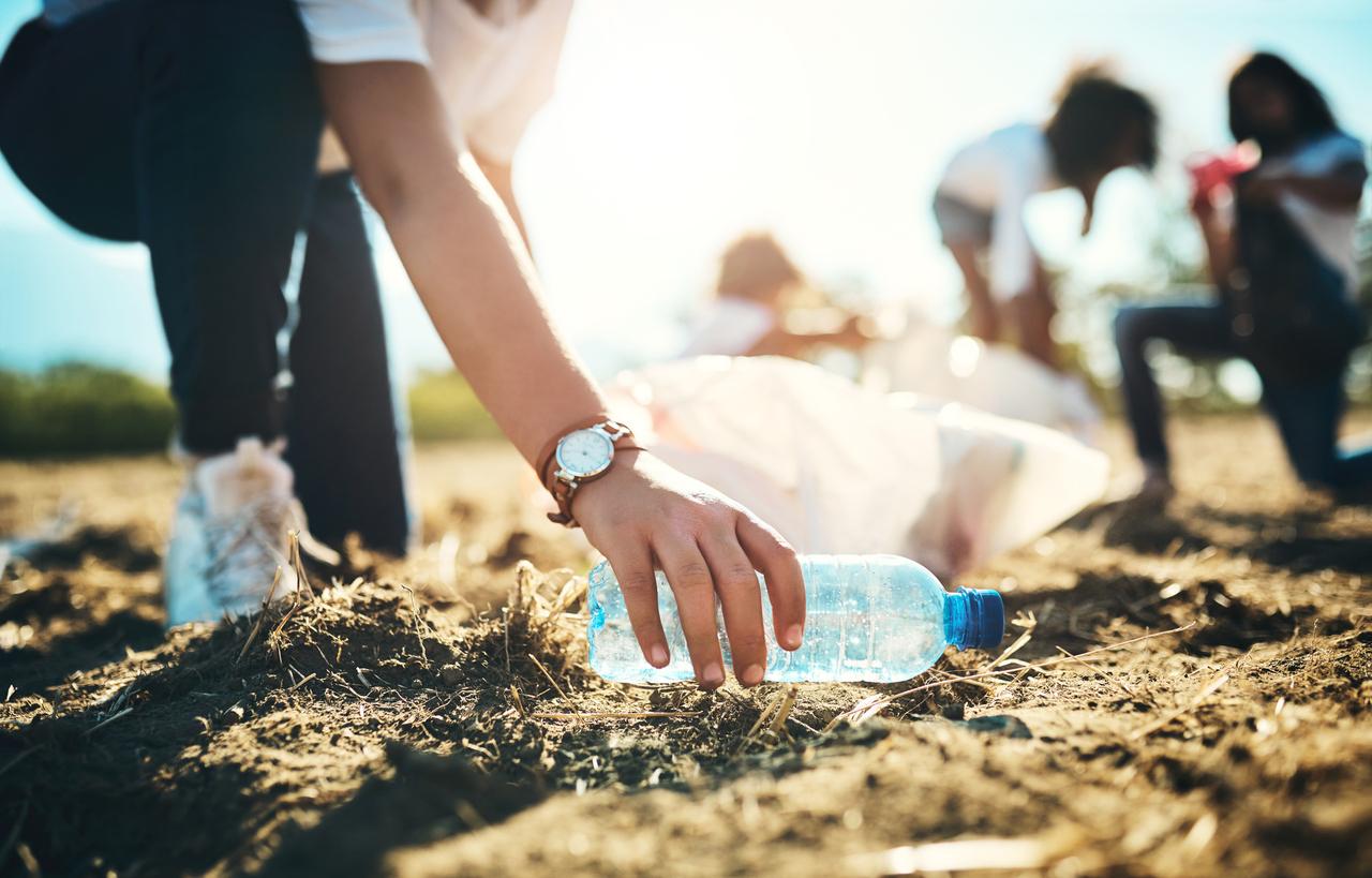 A volunteer wearing a watch picks up a plastic bottle from the ground.