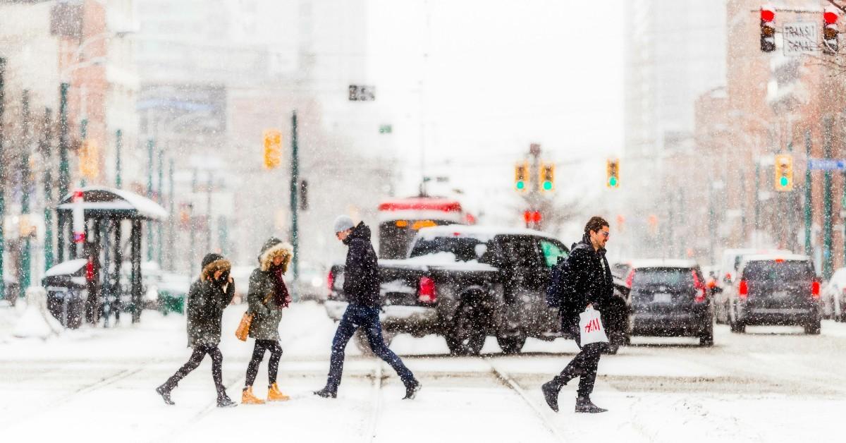 People cross a city street as snow begins to fall around them