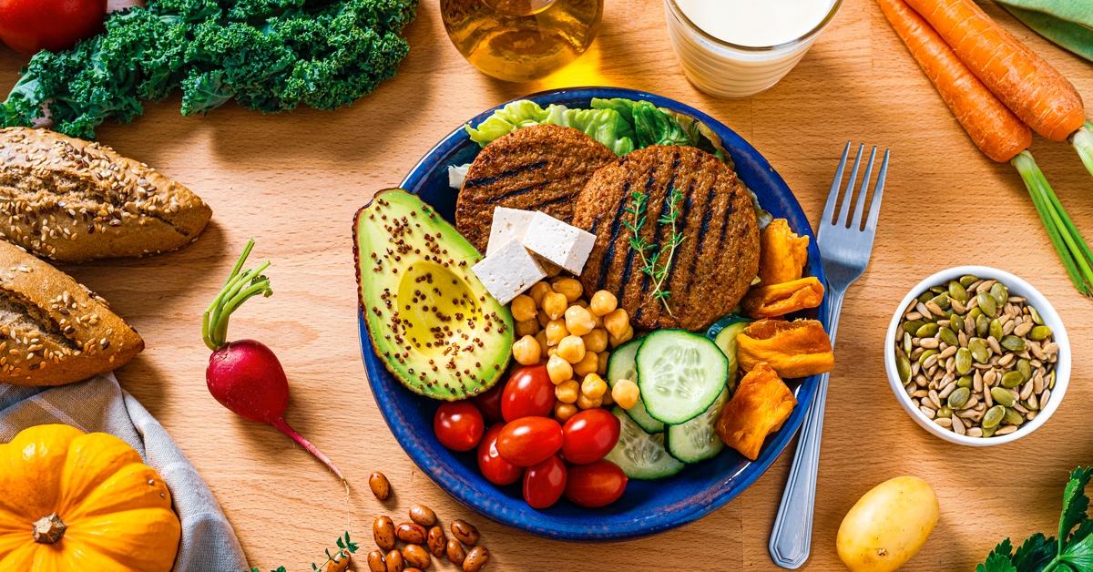 Full meal of vegan substitutes on a blue plastic plate, including soy burger patties, cherry tomatoes, tofu, chickpeas, and cucumbers.