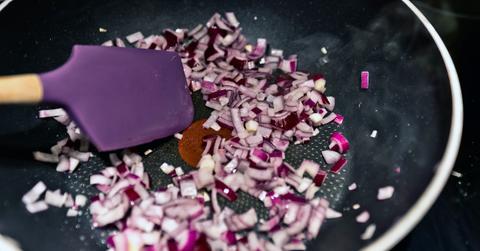 A purple spatula and diced onion in a frying pan