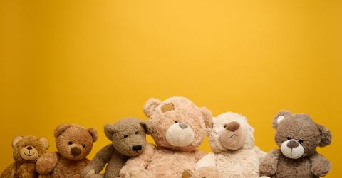 A group of teddy bears are pictured in a row in front of a yellow background,