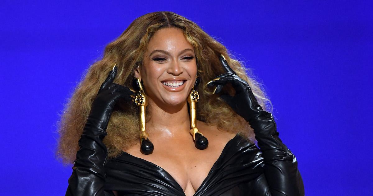 Beyoncé smiles at the 2021 Grammy Awards, in a black leather outfit in front of a blue background