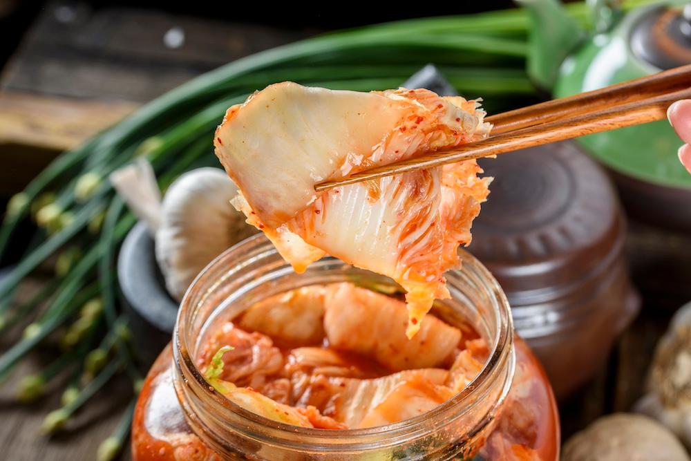 Someone using chopsticks to take kimchi out of a jar. 