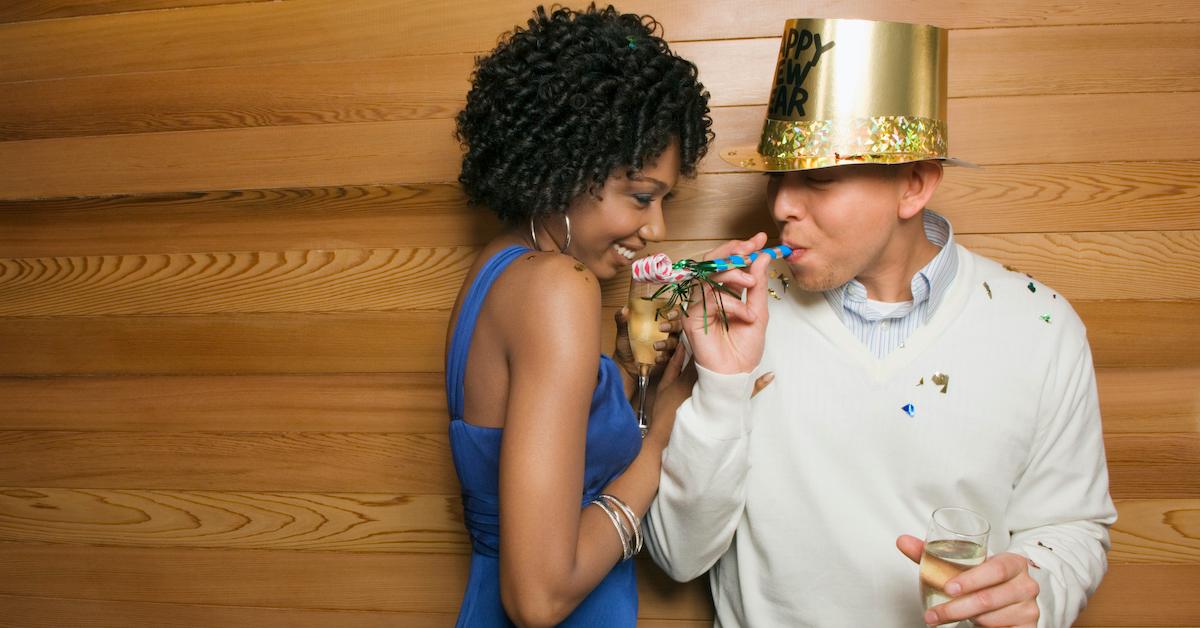 Two people celebrating New Year's Eve with confetti, drinks, and hats. 