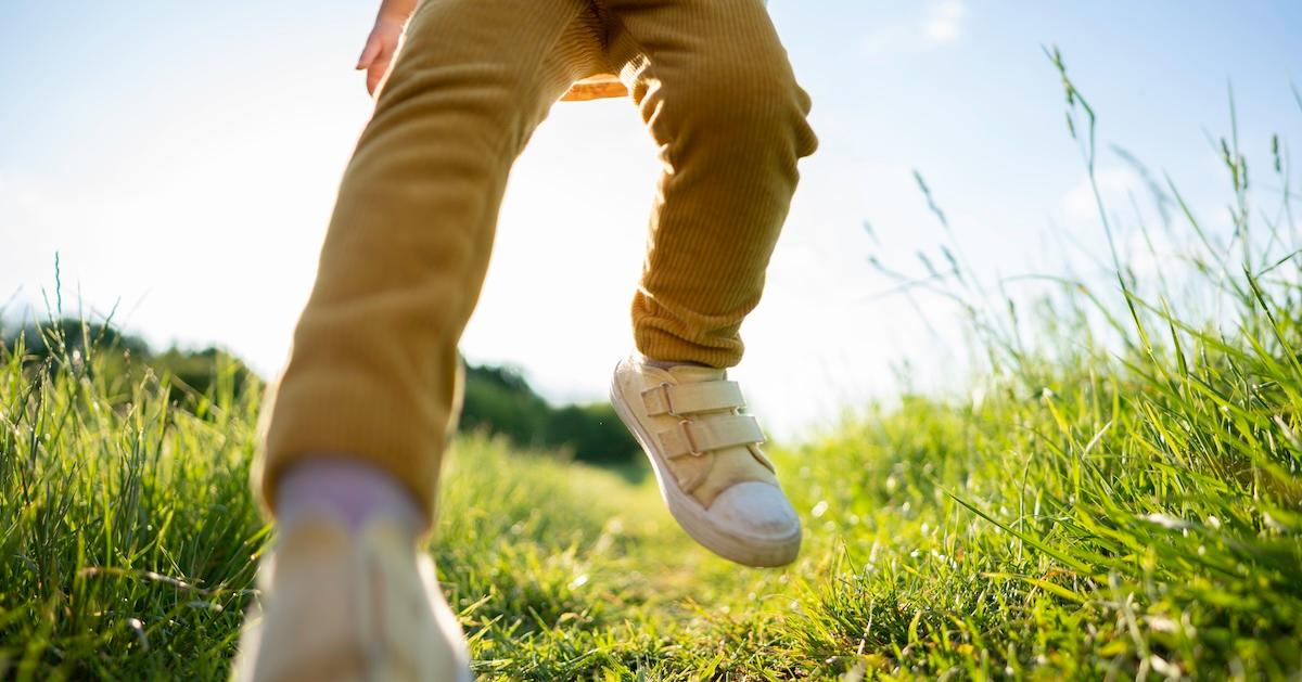 Lower half of child running through grass at sunset