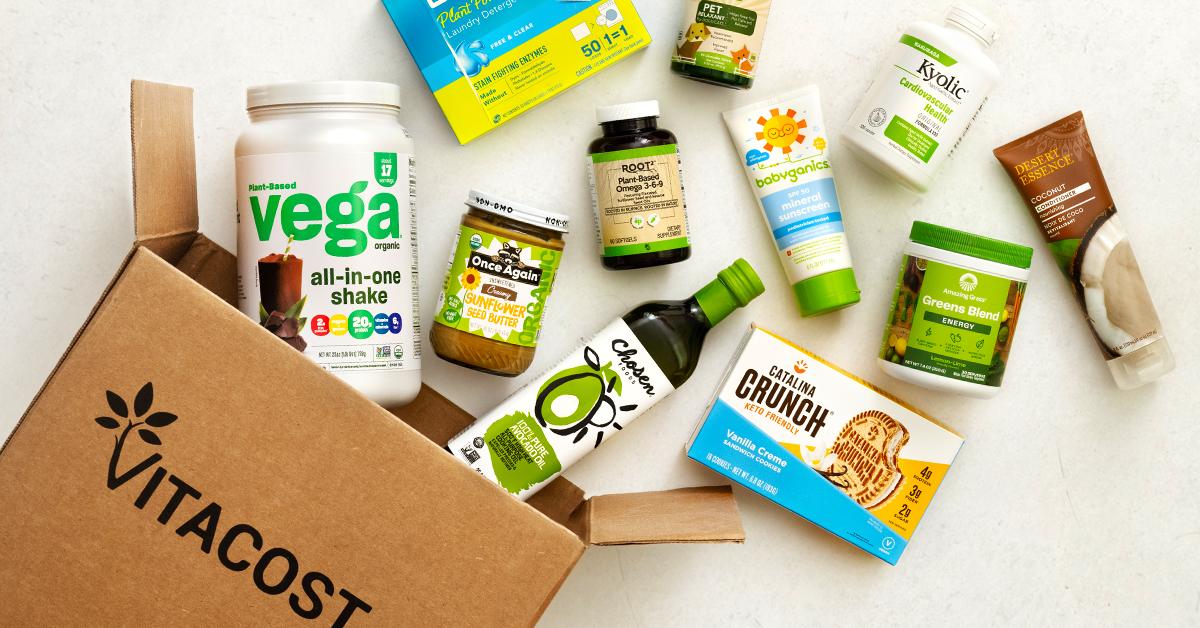 Cardboard Vitacost box on a white surface, with various natural food products coming out of it