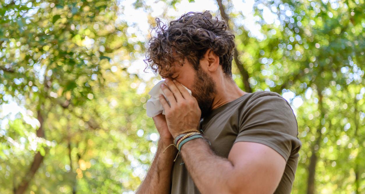 A man blowing his nose into a tissue outdoors.