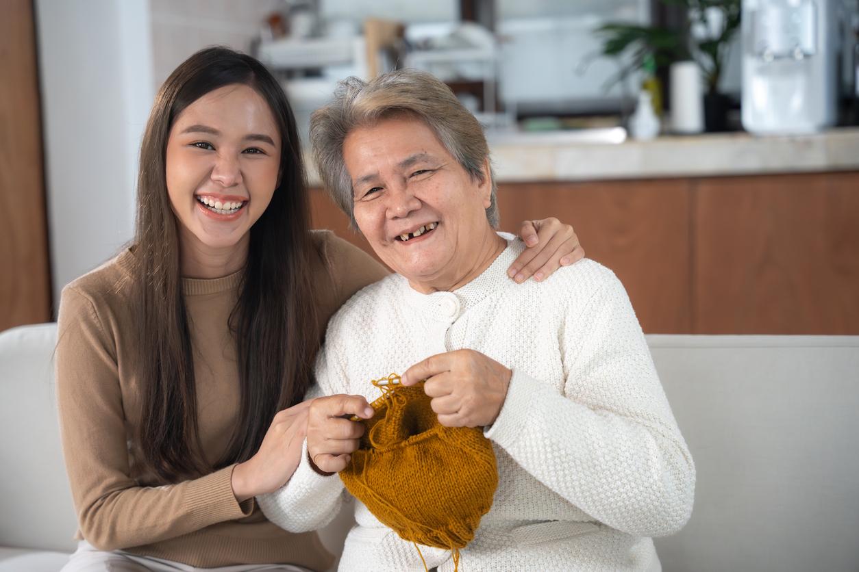 A young woman and her older family member smile together on the couch while holding a crochet project.