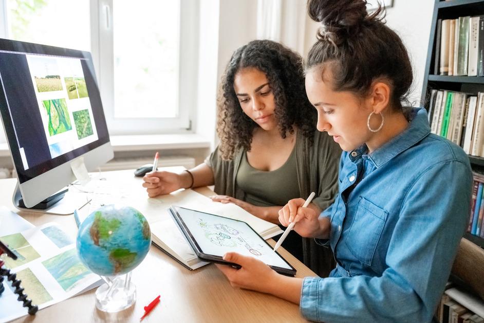 Two woman sit a desk with a computer while working on environmental assignments.