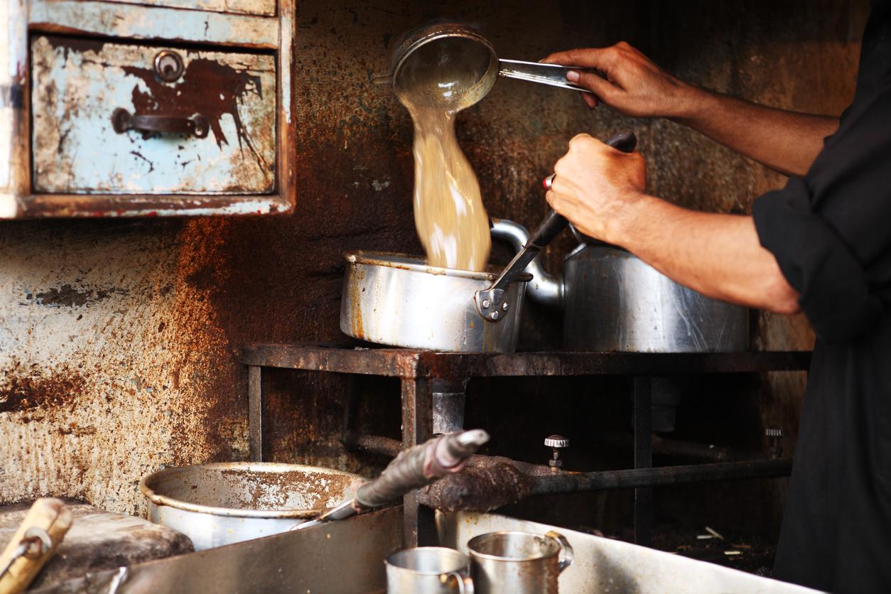 A chef in a black uniform in a kitchen creates a dirty chai concoction in a large pot intended for mass sale at a cafe.