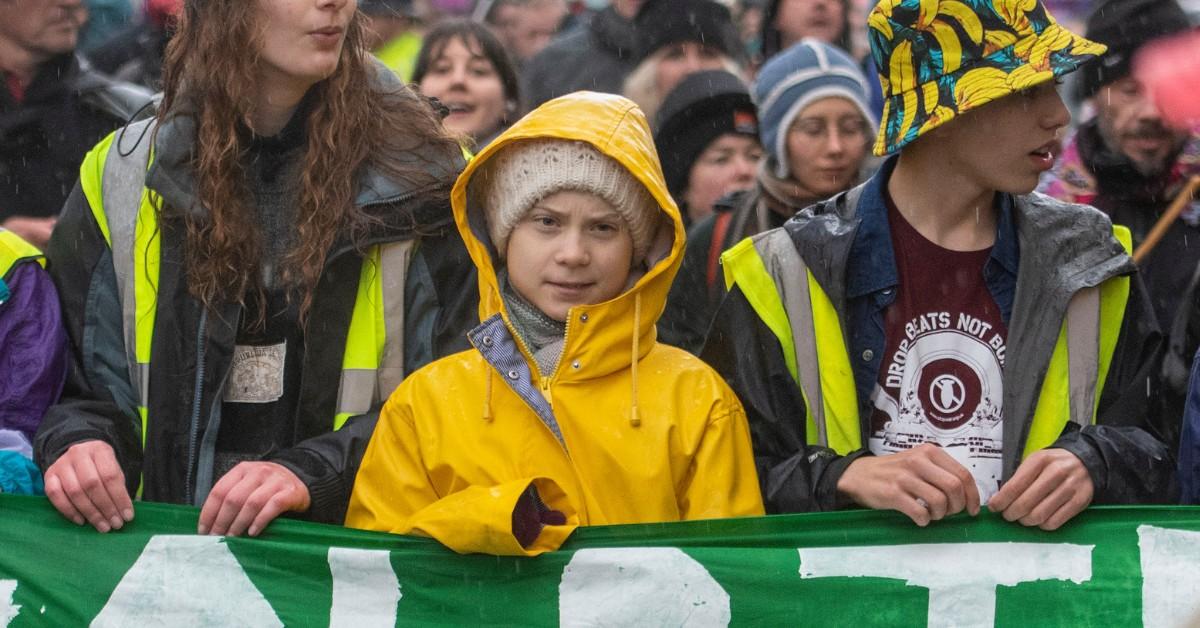 Greta Thunberg walks in a protest line while wearing a yellow rain jacket