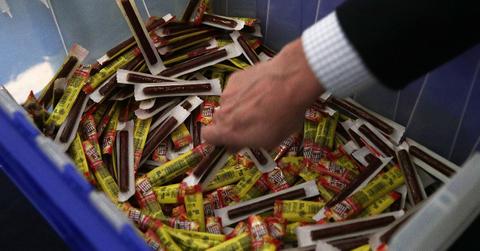 A man's hand grabs a Slim Jim from a pile of them.