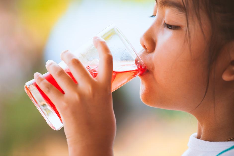 A young girl drinks a glass of red juice with ice. 