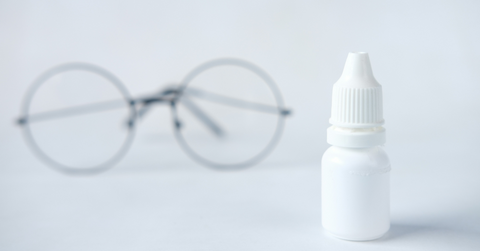 A bottle of eyedrops sits next to a pair of glasses