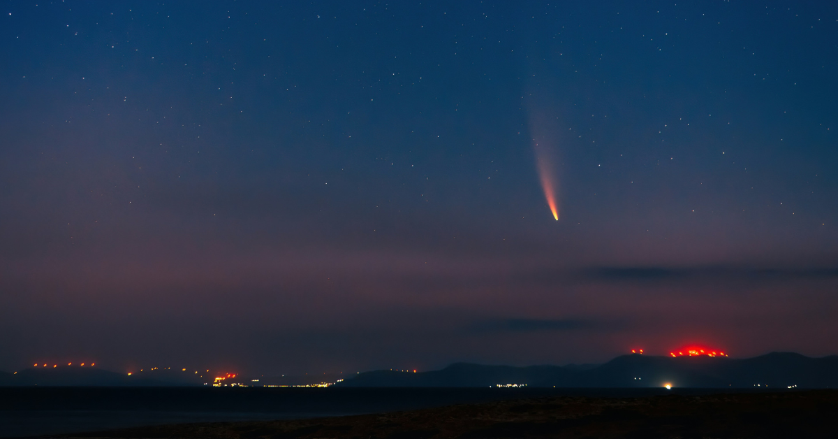 A meteor streaks across the night sky with mountains and lights in the distance