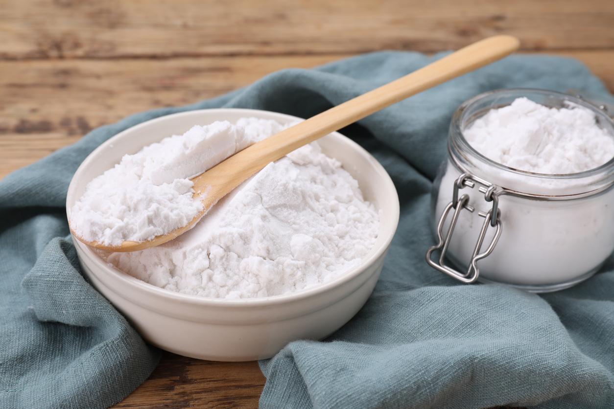 A bowl of cornstarch is pictured beside a jar of cornstarch atop a blue tablecloth on a wooden table.