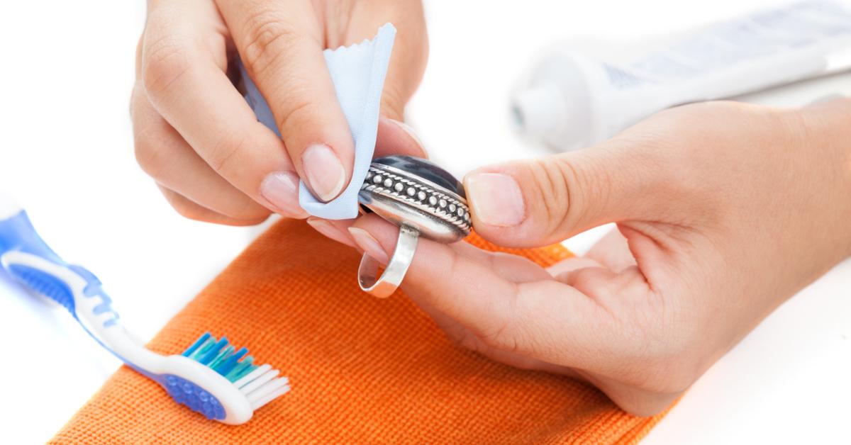 Close-up photo of hands cleaning a silver-toned ring with a cloth and a toothbrush 