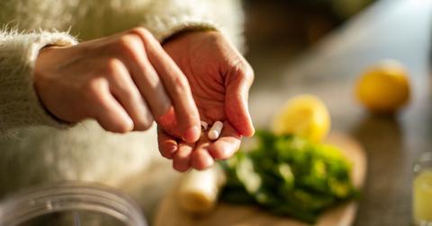 A person wearing a white sweater holds a few supplements with produce on the counter below.