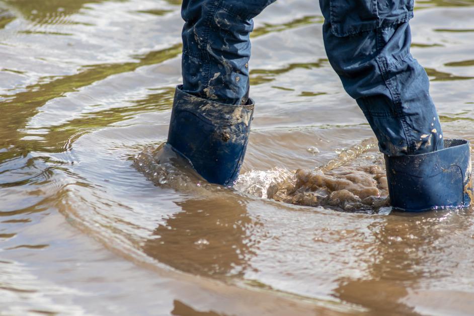 A person wearing rain boots and long pants walks through floodwaters.  