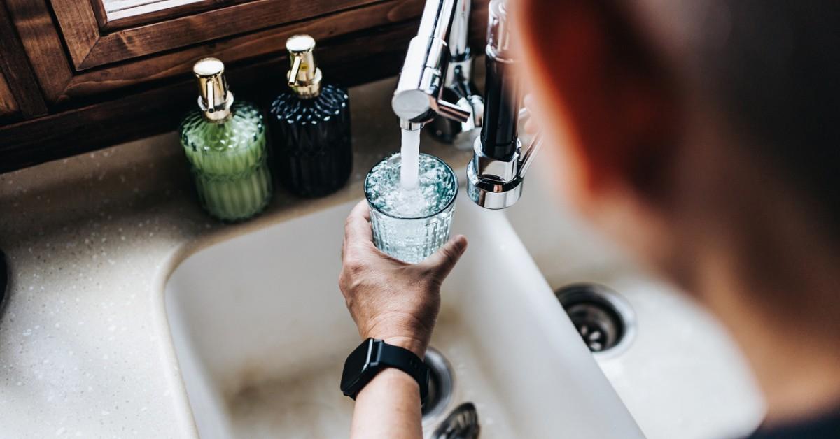 An over-the-shoulder perspective of someone filling their glass with tap water