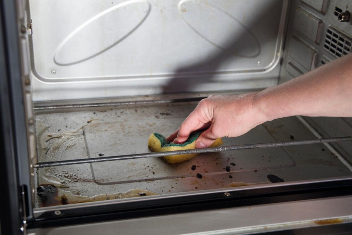 person scrubbing dirty oven with a sponge