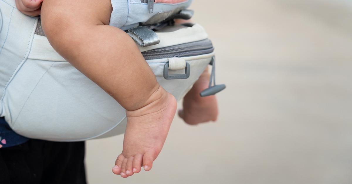 baby's feet dangling from a diaper bag carrier