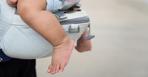 baby's feet dangling from a diaper bag carrier