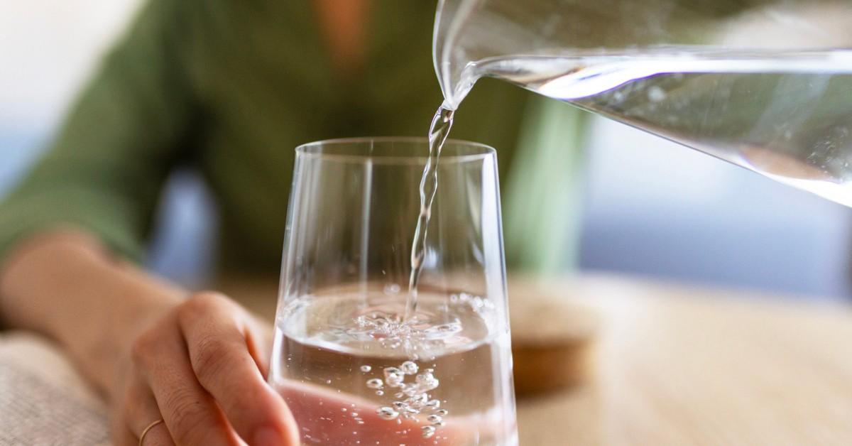 A woman pours water into a glass from a clear pitcher