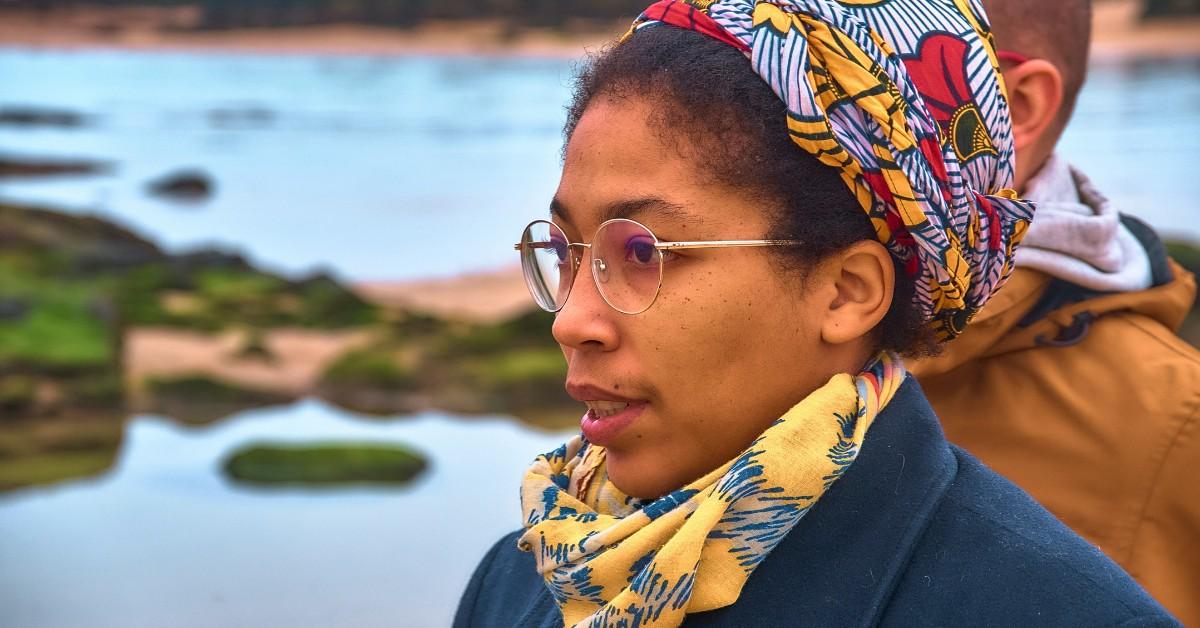 A woman wearing glasses stands next to a lake