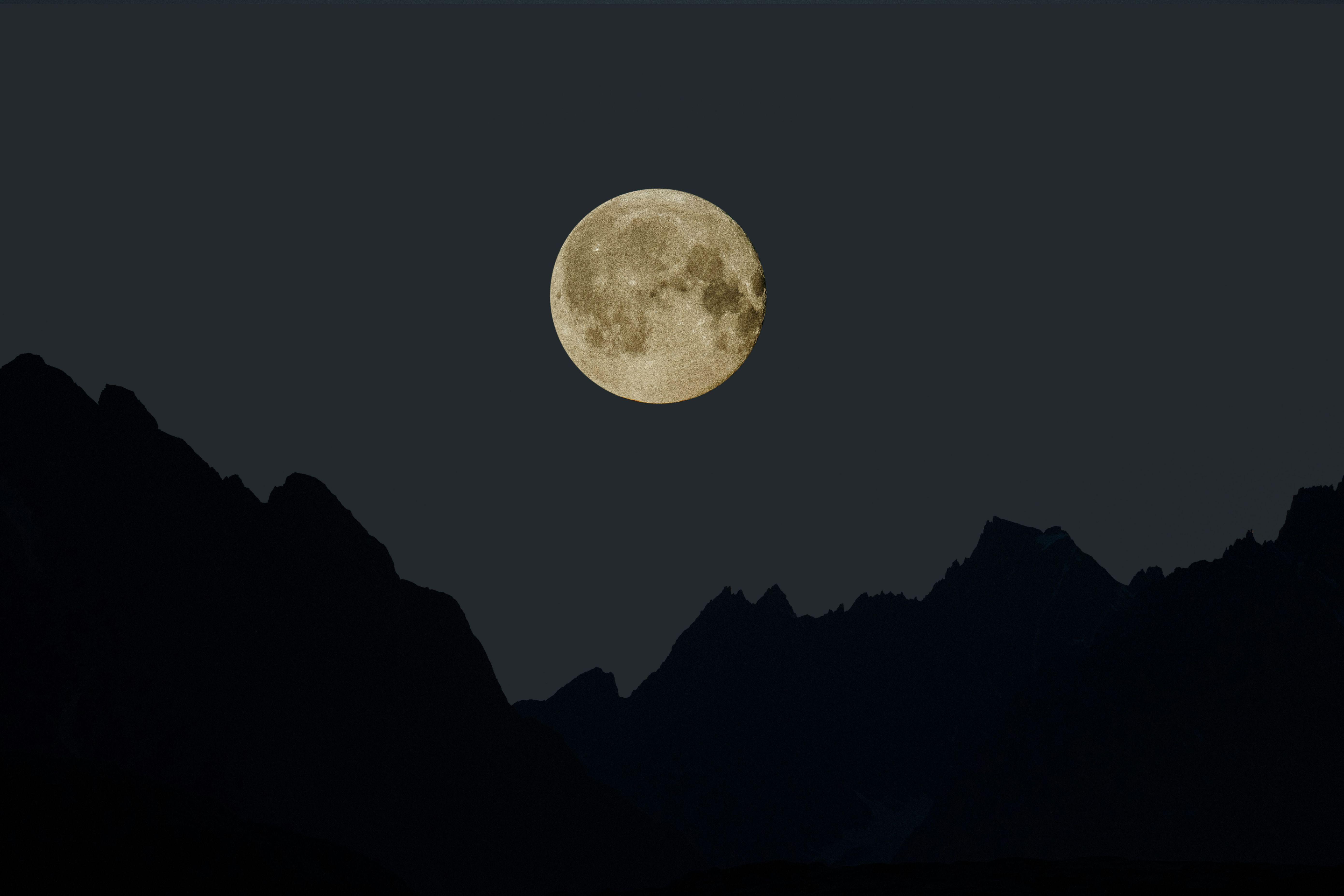 A full moon appears over a silhouette of mountains.