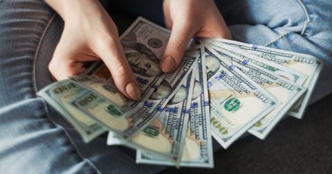 A woman holds nine 100 dollar bills out like a fan