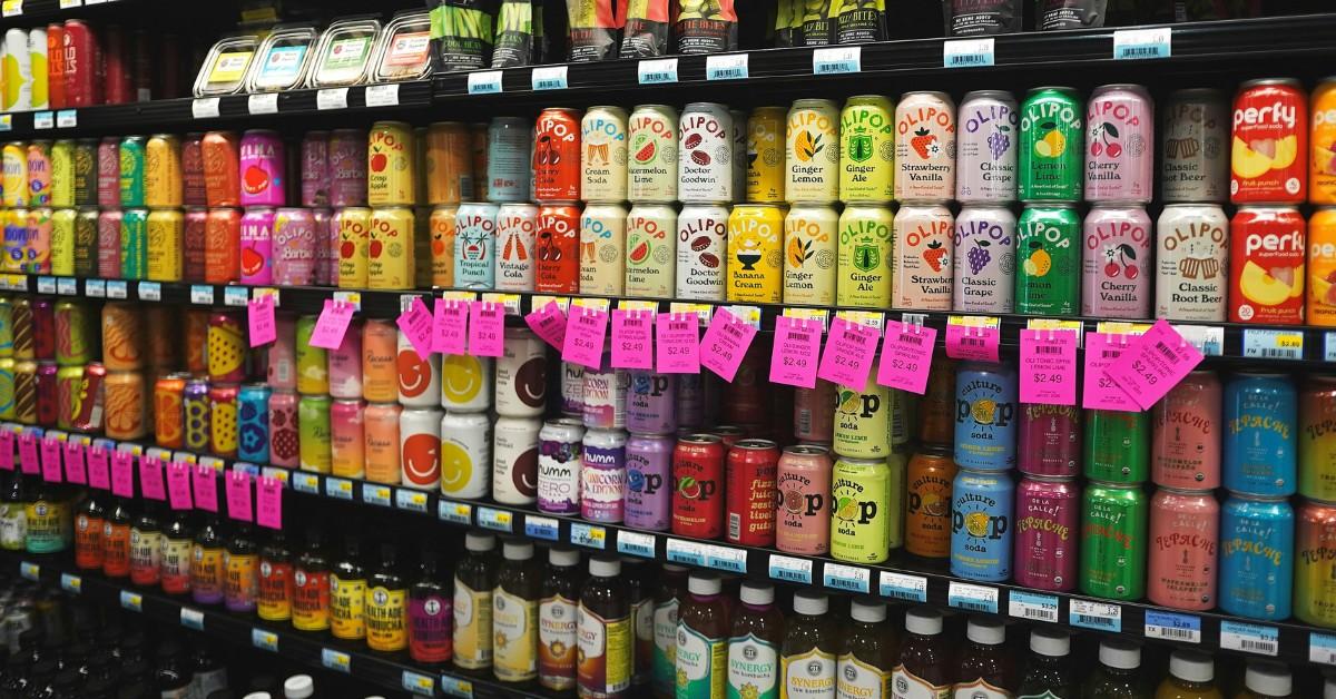 A grocery store shelf is filled with a variety of prebiotic drinks like Olipop and Poppi