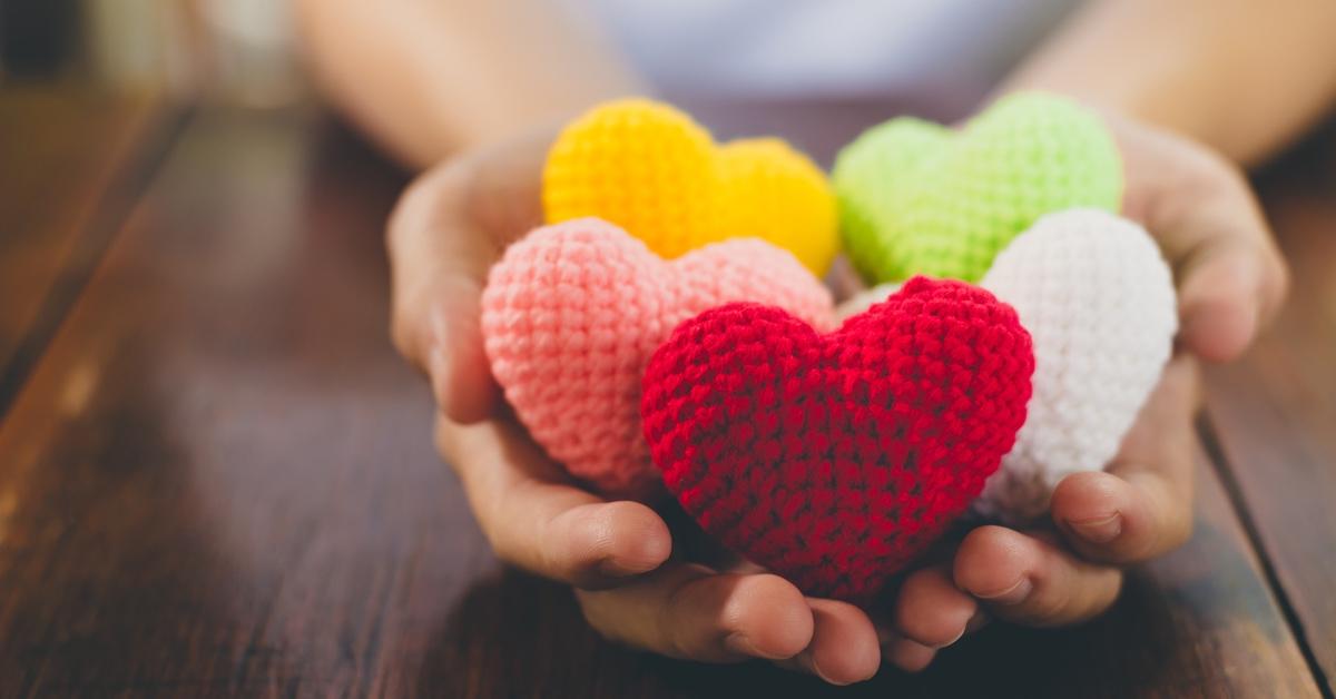 Person with hands full of crochet hearts in pink, red, and white leaning on a table.