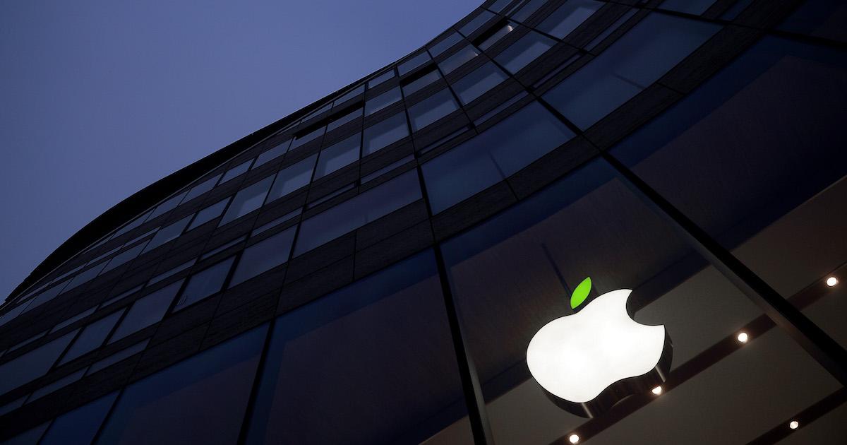 The facade of an Apple store shows the white Apple logo with an illuminated green leaf.