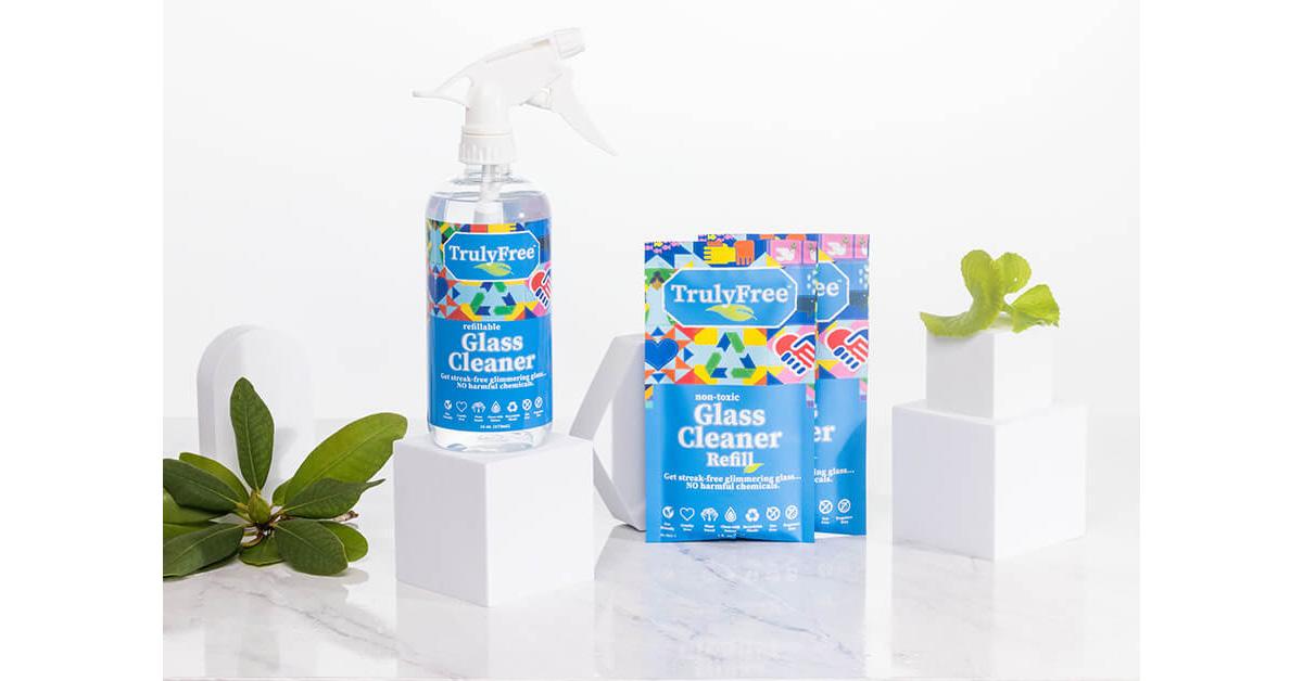 bottle of glass cleaner with two refill packages on a marble surface with plants