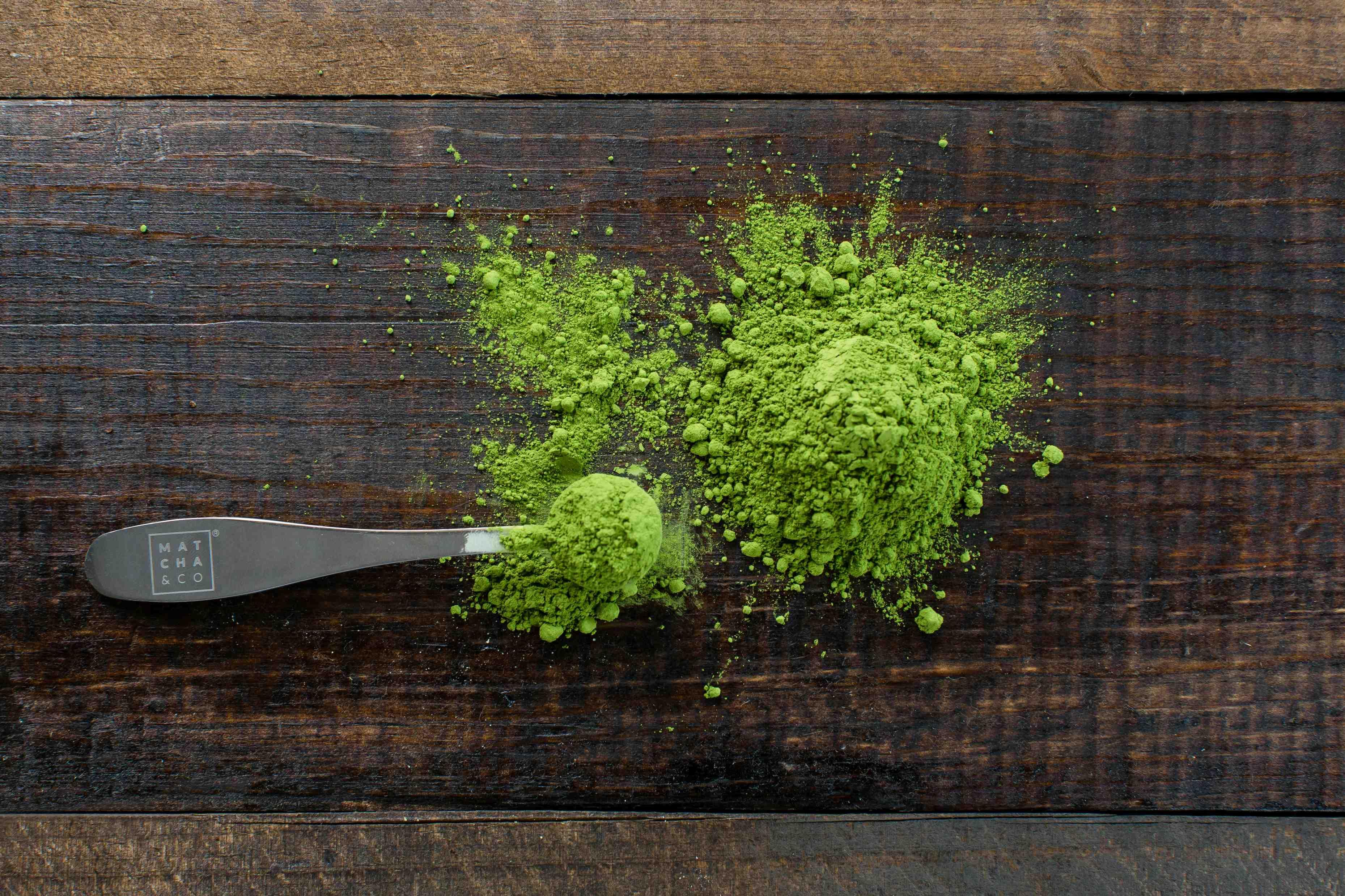 A scoop of green powder is pictured in the center of a wooden chopping block.