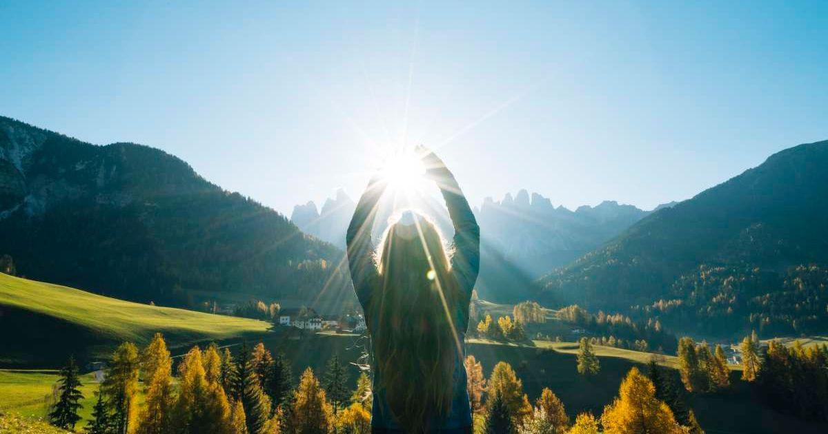 A woman reaches for the sun overlooking the valley and mountains. (Representative Cover Image Source: Getty Images | Ascent/PKS Media Inc.)
