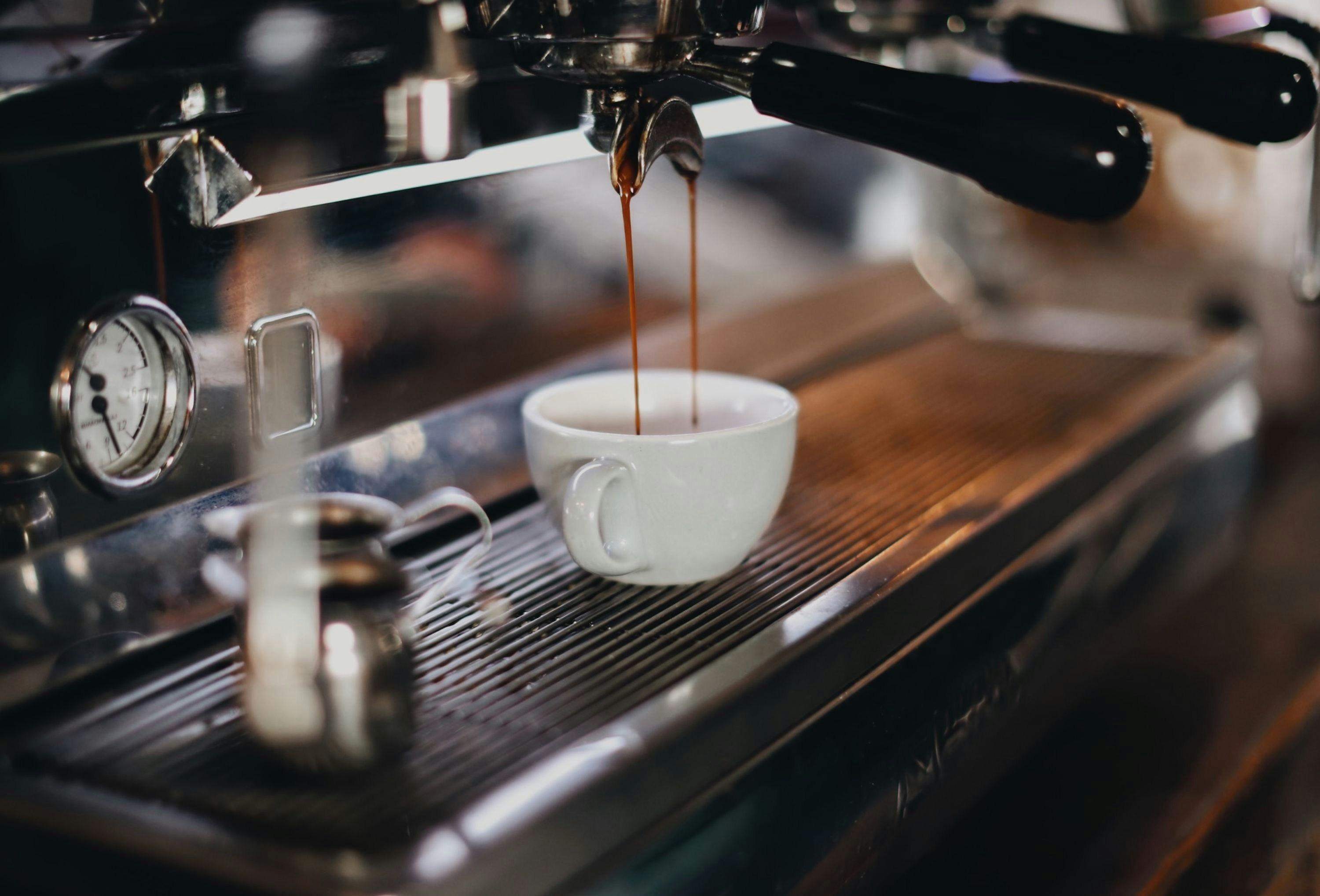 A ceramic white coffee cup is pictured atop a coffee machine being filled with espresso.