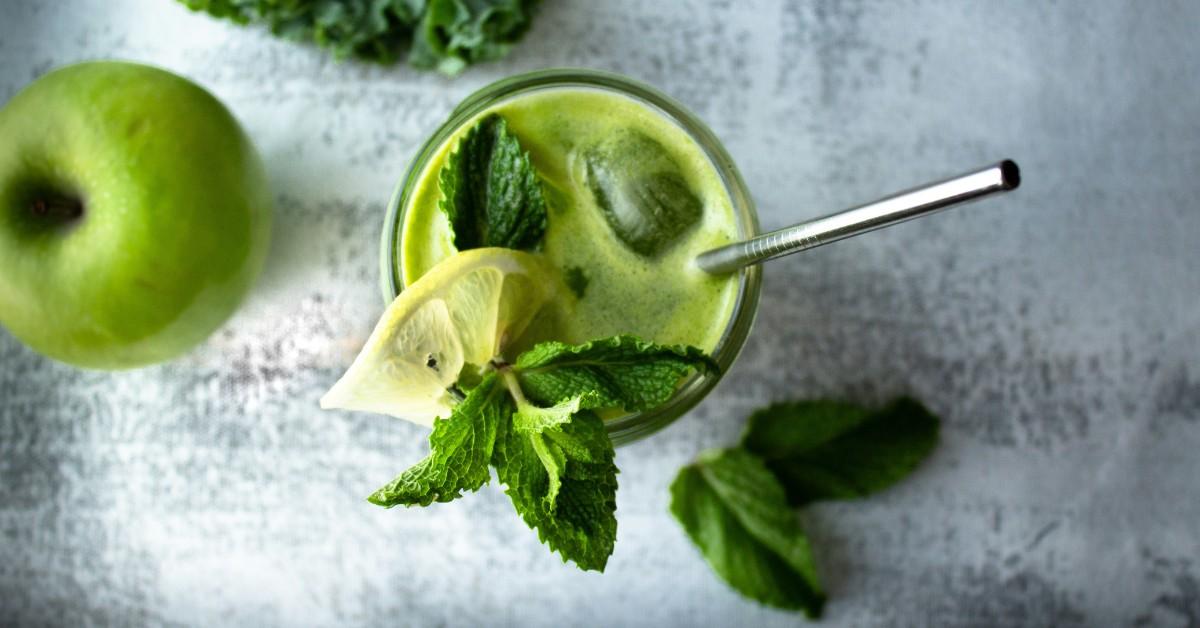 A cup of green juice is topped off with a sprig of mint and a wedge of lime