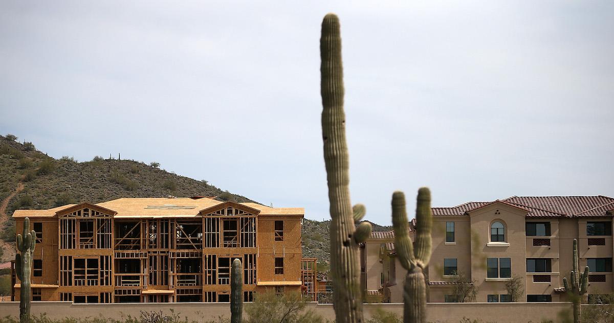 Cacti sit in the foreground, while a house under construction sits next to a built house, in Phoenix, Ariz.