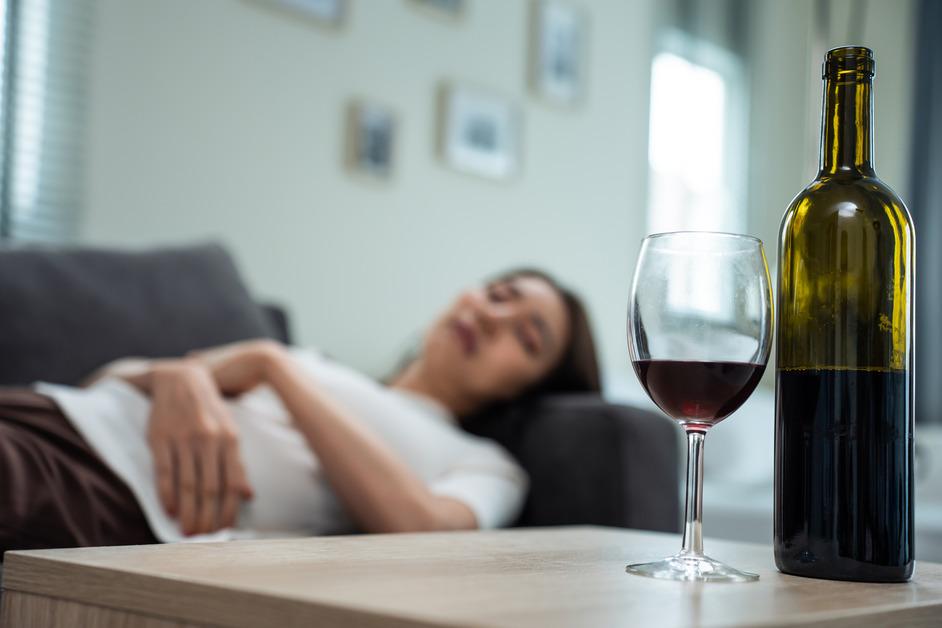 Woman lies down on the couch while she stares at a glass of wine next to the bottle on the table. 