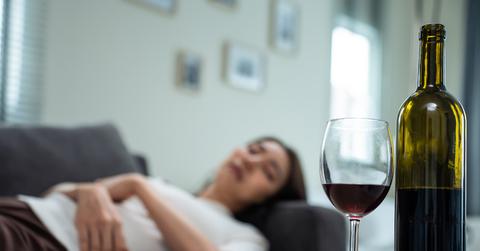 Woman lies down on the couch while she stares at a glass of wine next to the bottle on the table.