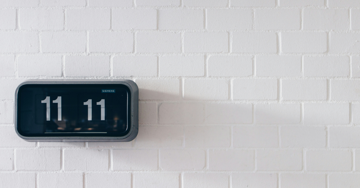 An analogue clock mounted on a white brick wall reads 11:11